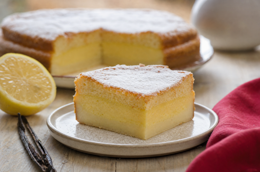 Fetta di torta magica al limone e vaniglia con i tre strati, spolverata di zucchero a velo